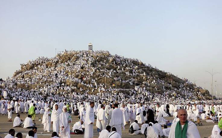 Jemaah haji berkumpul di Padang Arafah, mengenakan pakaian ihram, berdoa dengan khusyuk di bawah langit terbuka saat wukuf, momen puncak ibadah haji yang penuh makna dan keutamaan.