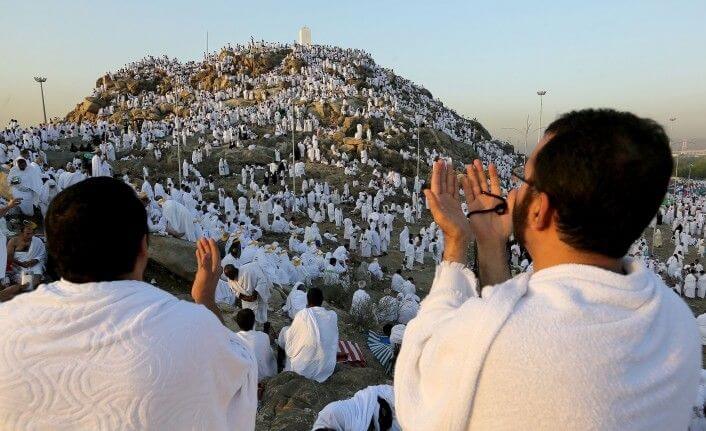Jemaah haji sedang khusyuk berdoa di Padang Arafah, mengenakan pakaian ihram, dengan latar belakang langit terbuka dan suasana penuh kekhidmatan dalam puncak ibadah haji.