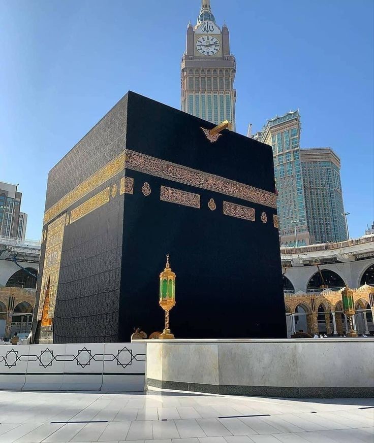 Foto Ka'bah megah berdiri di tengah Masjidil Haram, dikelilingi oleh lantai marmer putih dan suasana yang khusyuk. Struktur hitam persegi dengan Kiswah hitam berhiaskan kaligrafi emas, menjadi pusat perhatian umat Muslim dari seluruh dunia.